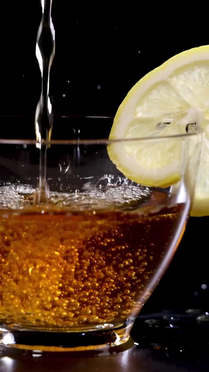 Un getto di tè viene versato in una tazza di vetro con una fetta di limone, su uno sfondo scuro.