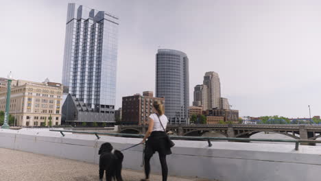 young woman walking her dog takes in the view from a bridge in an urban downtown setting