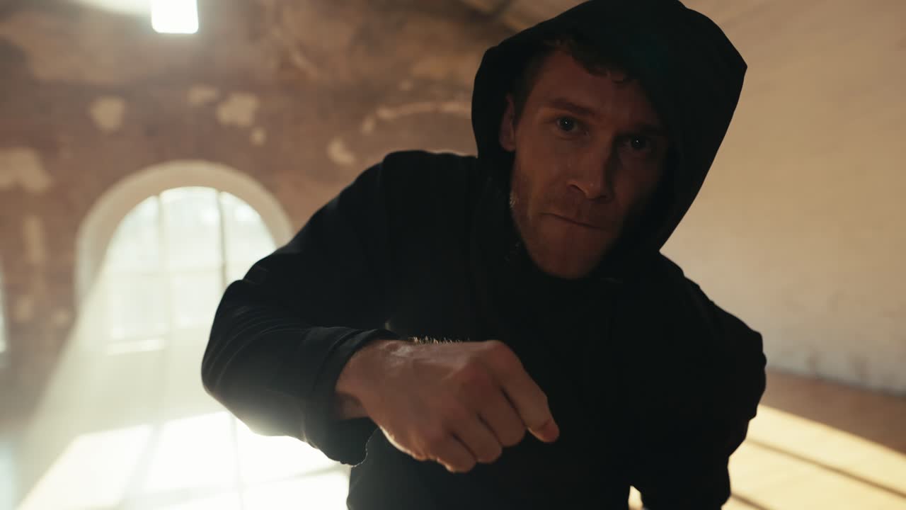 첫 번째 사람으로부터 근접 촬영, 후드와 함께 검은 스포츠 유니폼을 입은 남성 운동 선수가 그의 타격을 연습합니다.