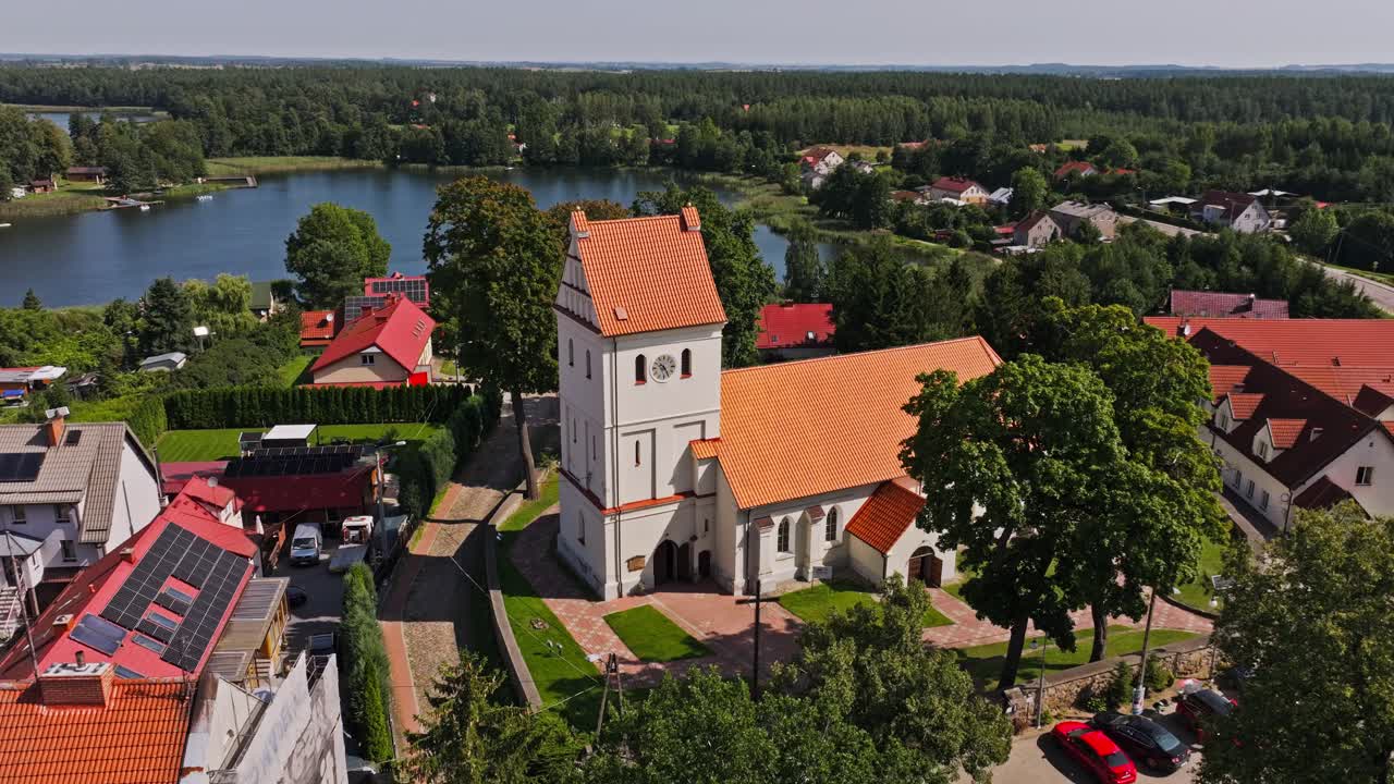 Smooth aerial motion near lakeside church in Wydminy surrounded by trees
