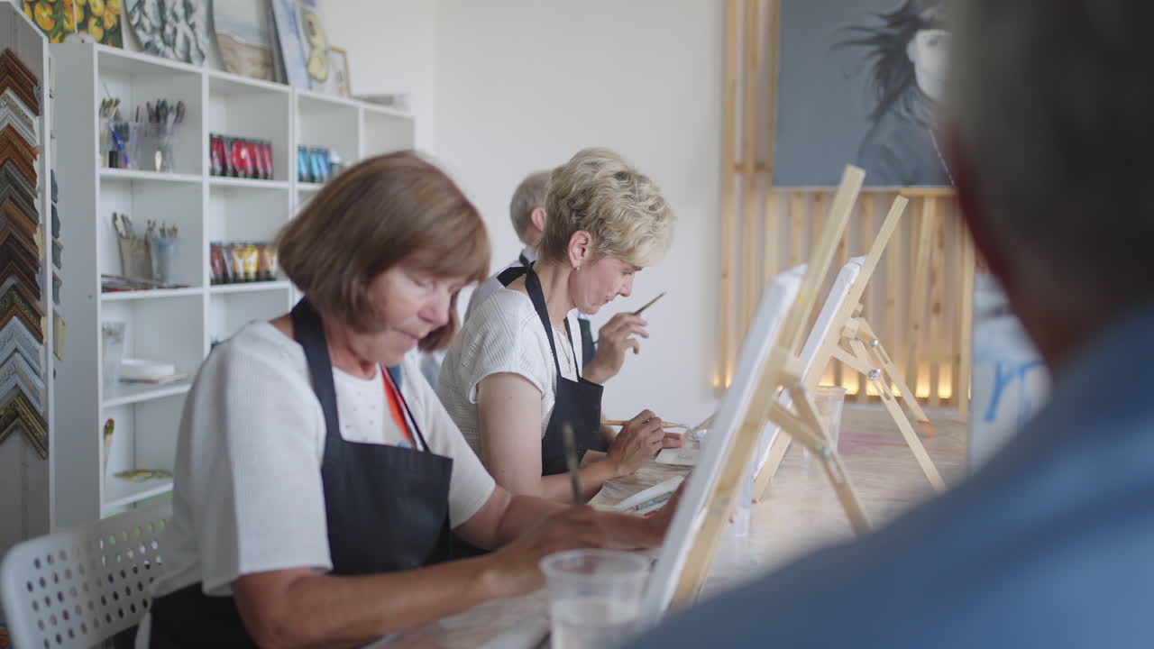 De docent geeft tekenles aan een groep gepensioneerde vrienden. Een groep oudere mannen en vrouwen tekent samen en glimlacht.