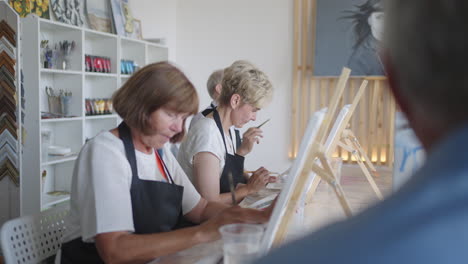 the teacher shows a group of friends of retired people in the elderly at drawing courses. a group of elderly men and women draw together and smile