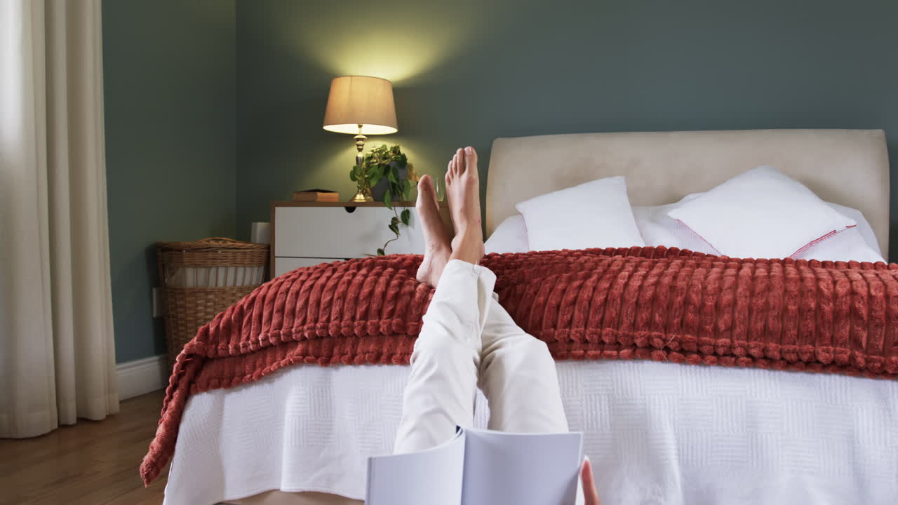 Relaxing at home, woman reading book with feet up on bed
