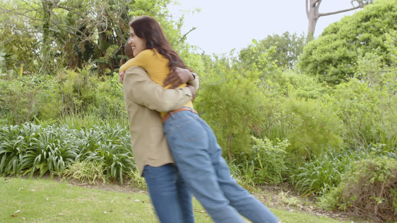 Diverse multiracial couple embracing joyfully in lush green park, celebrating togetherness