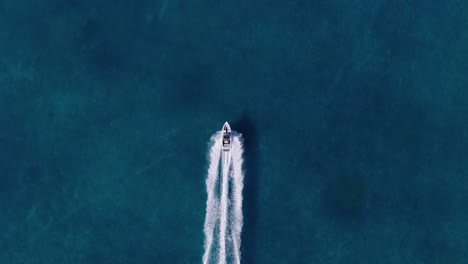 top down tracking aerial follows speed boat and white wash wake in cerulean blue ocean water