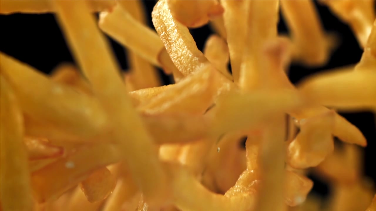 Caduta al rallentatore di patatine fritte dorate su sfondo nero