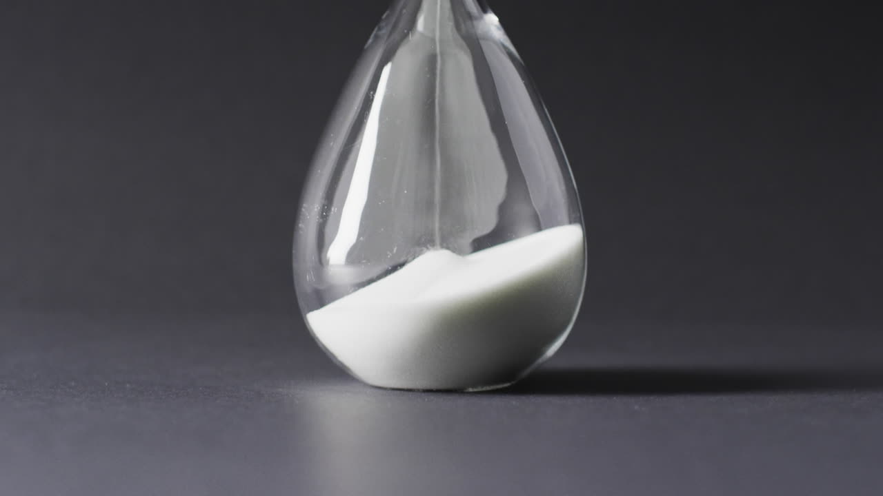 Video of close up of hourglass with sand pouring, copy space on black background