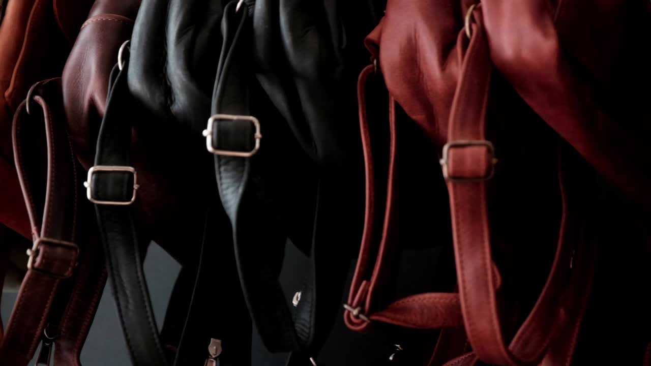 다양한 색의 손으로 만든 가죽 가방, 줄무와 줄이 판매되는 랙에 매달려 있습니다.