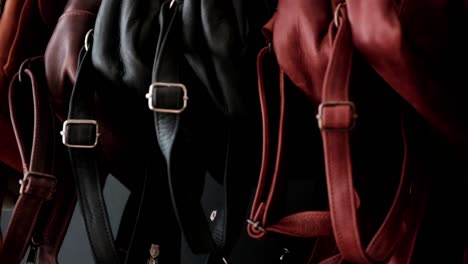una variedad de bolsas de cuero hechas a mano de diferentes colores con correas y hebillas colgadas en un estante para la venta