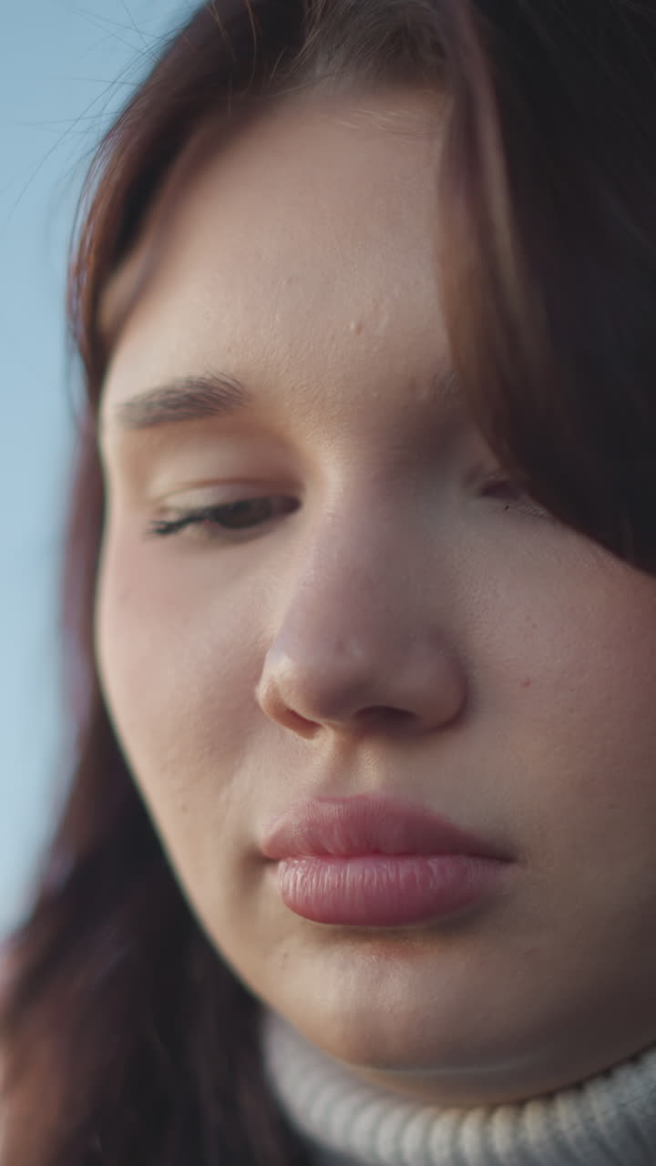 은 입술, 약간 아래로 내려진 눈, 코 반지, 사려 깊은 표정으로 초점을 맞추고, 바람에 날아다니는 머리카락, 부드러운 자연 빛, 흐릿한 배경