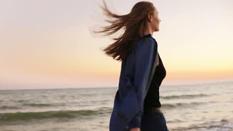 Young-beautiful-woman-running-by-the-sea-during-sunset-and-holding-burning-sparkling-candles-in-both-hands.-Slow-Motion-shot