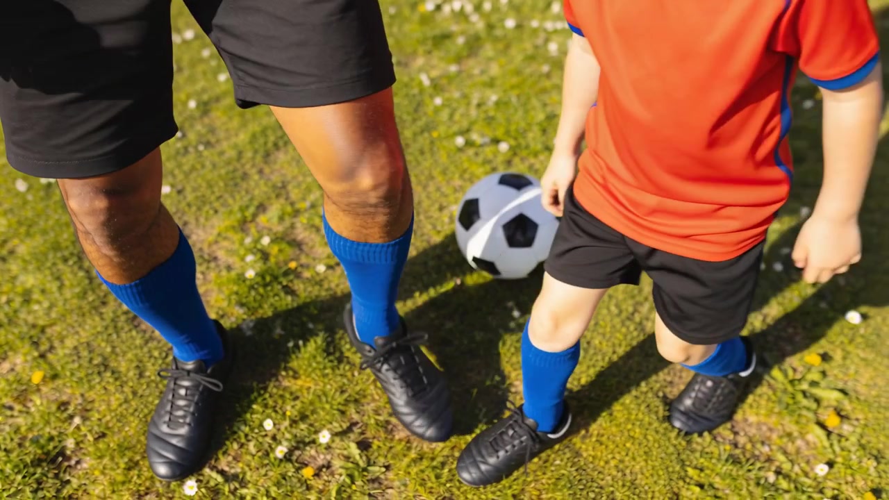 L'allenatore in maglietta blu si prepara stringendo i tacchetti del bambino in maglia rossa sull'erba, con un pallone da calcio.