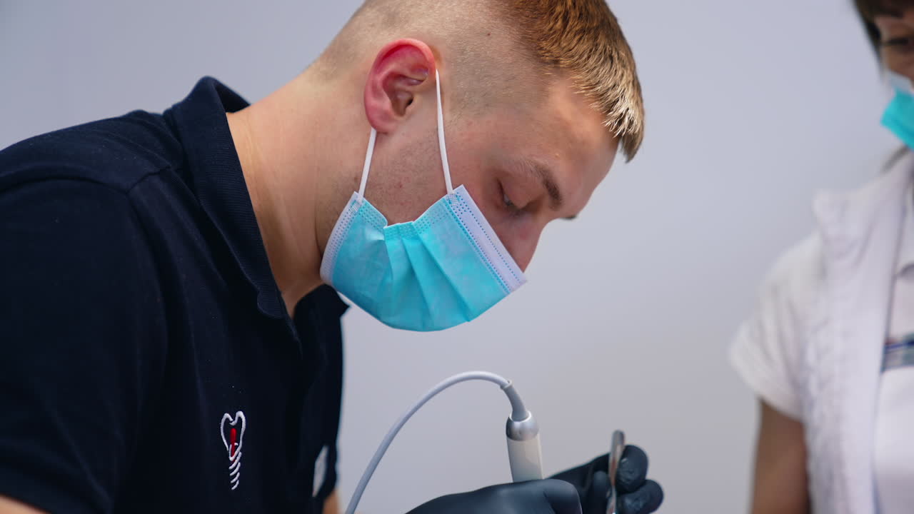 Dentist and a nurse in protective masks work in clinic. Professional male stomatologist treating teeth with dental tools. Work of dentist. Healthcare and medicine concept. Close-up.