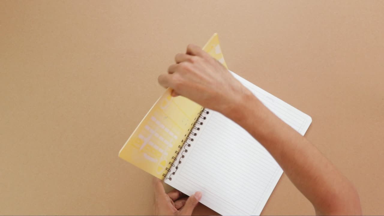 Hands removing covers from a spiral notebook, overhead view