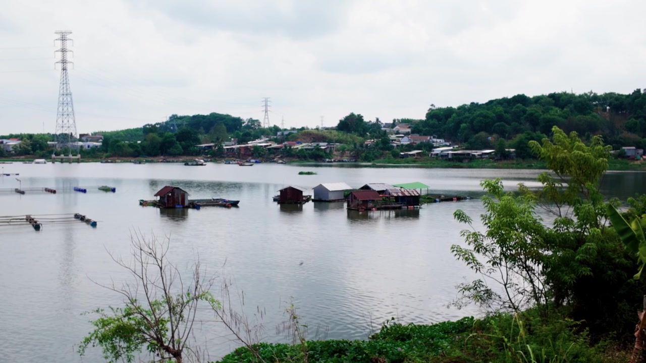 Il ponte La Nga attraversa il fiume, offrendo viste di case su palafitte e colline verdi. Barche galleggiano sull'acqua, mentre i cavi elettrici punteggiano il paesaggio. Questa vista cattura la vita quotidiana lungo il fiume