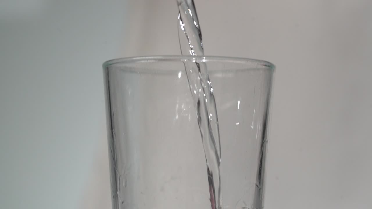 close-up mulher derramando líquido claro de jigger de metal em vidro alto claro em câmera lenta