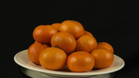 Orange-pyramid-of-Mandarin-Clementine-fruit-rotates-on-white-plate