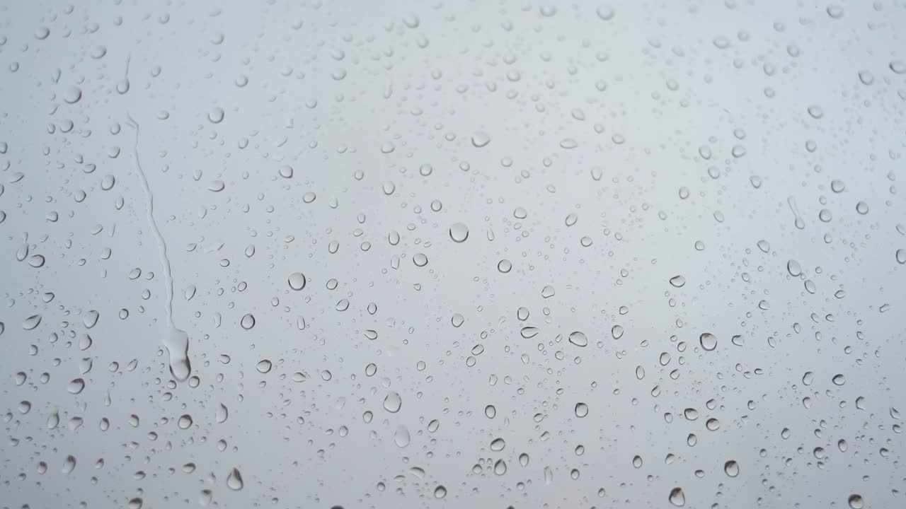 se ve a través de un vidrio de ventana una filmación cercana en cámara lenta de fuertes gotas de lluvia