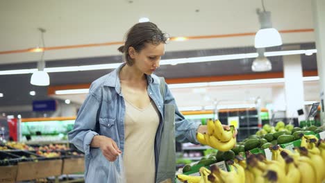 Handheld-Aufnahmen-Eines-Hübschen-Jungen-Mädchens-Im-Hemd,-Das-Im-Supermarkt-Früchte-Auswählt.-Legt-Einige-Bananen-In-Eine-Zellophantüte.-Konzentriert.-Legerer-Stil