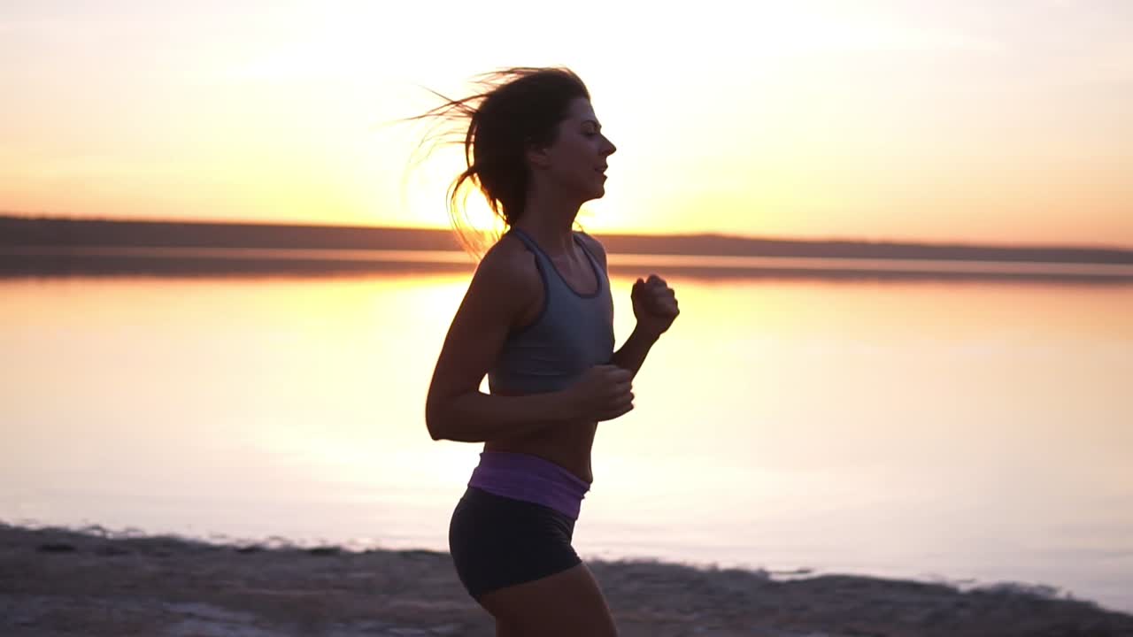 primer plano de una hermosa chica deportiva corriendo a lo largo del mar o lago en ropa deportiva. vista lateral