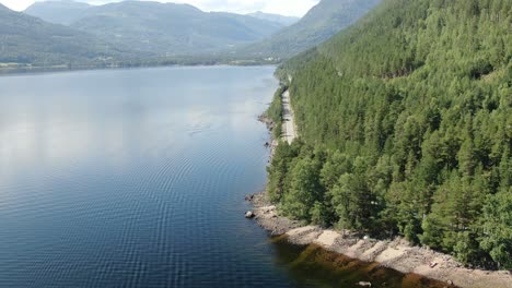 slow aerial shot of a road very close to the lake in the mountains