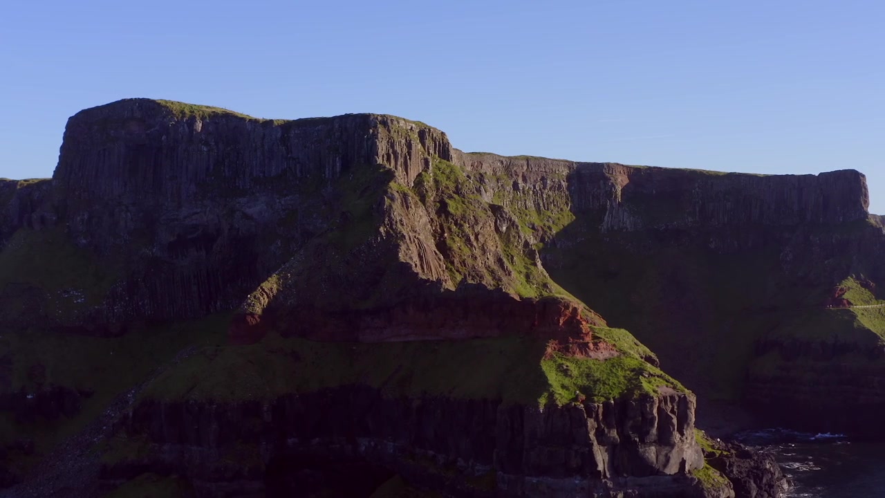 Dynamisk luftfoto-tilt, der afslører Amfiteatrets klipper og karakteristiske klippeformationer ved Giant's Causeway.