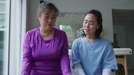 asian female physiotherapist helping female patient exercise arms with dumbbells at surgery