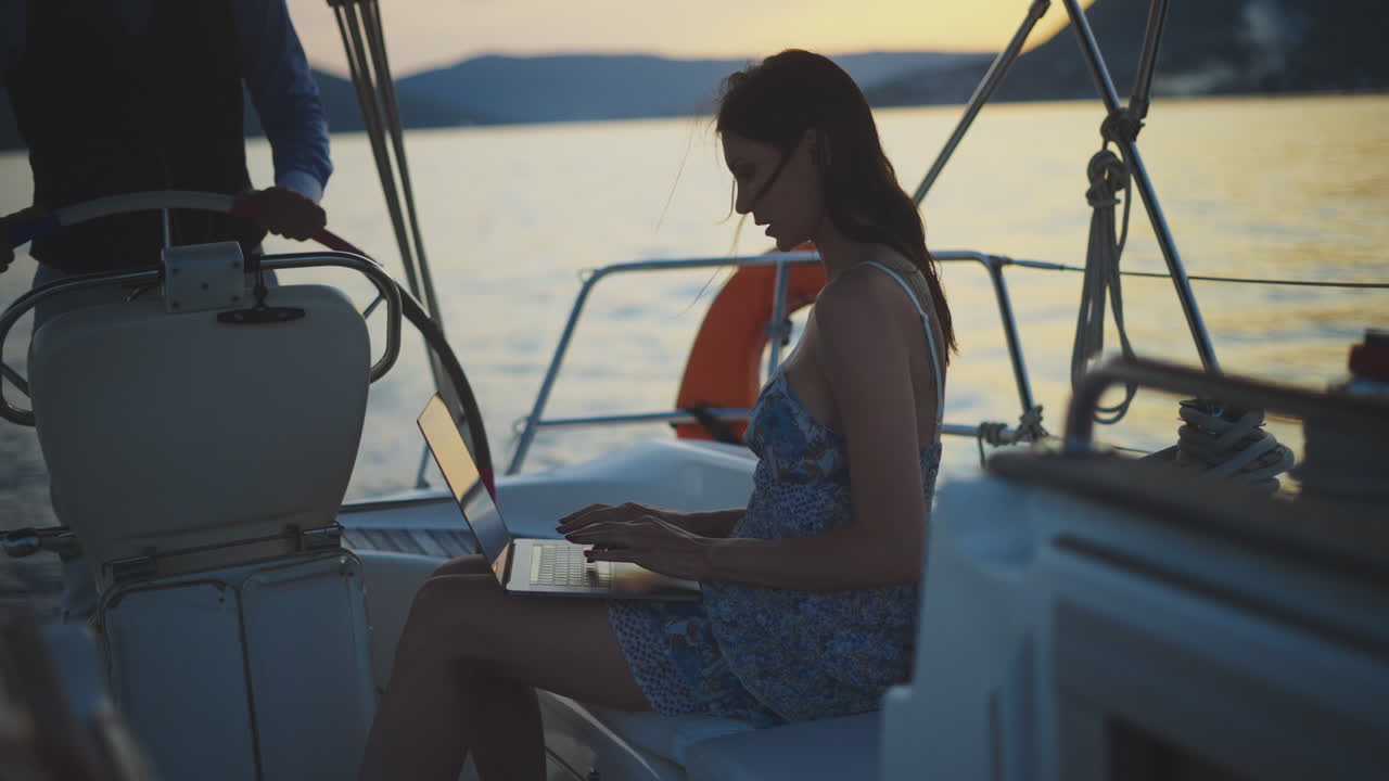 mujer trabajando en una computadora portátil en un yate al atardecer