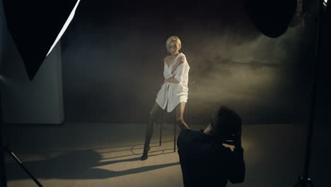 high angle view of caucasian young female model posing in the dark studio while the photographer taking shots of her