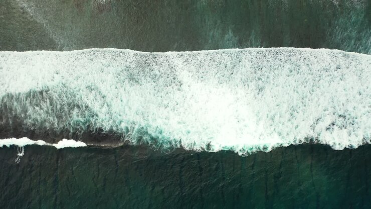 Aerial of a small white wave breaking and crashing in the middle of the dark blue ocean