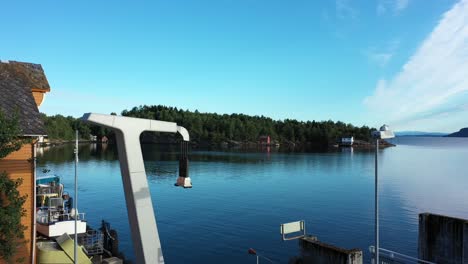 Electrical-high-voltage-ferry-charging-tower---Aerial-approaching-and-passing-charger---Cables-and-plug-hanging-down-ready-for-use---Early-sunny-day-morning-at-Utbjoa-Norway