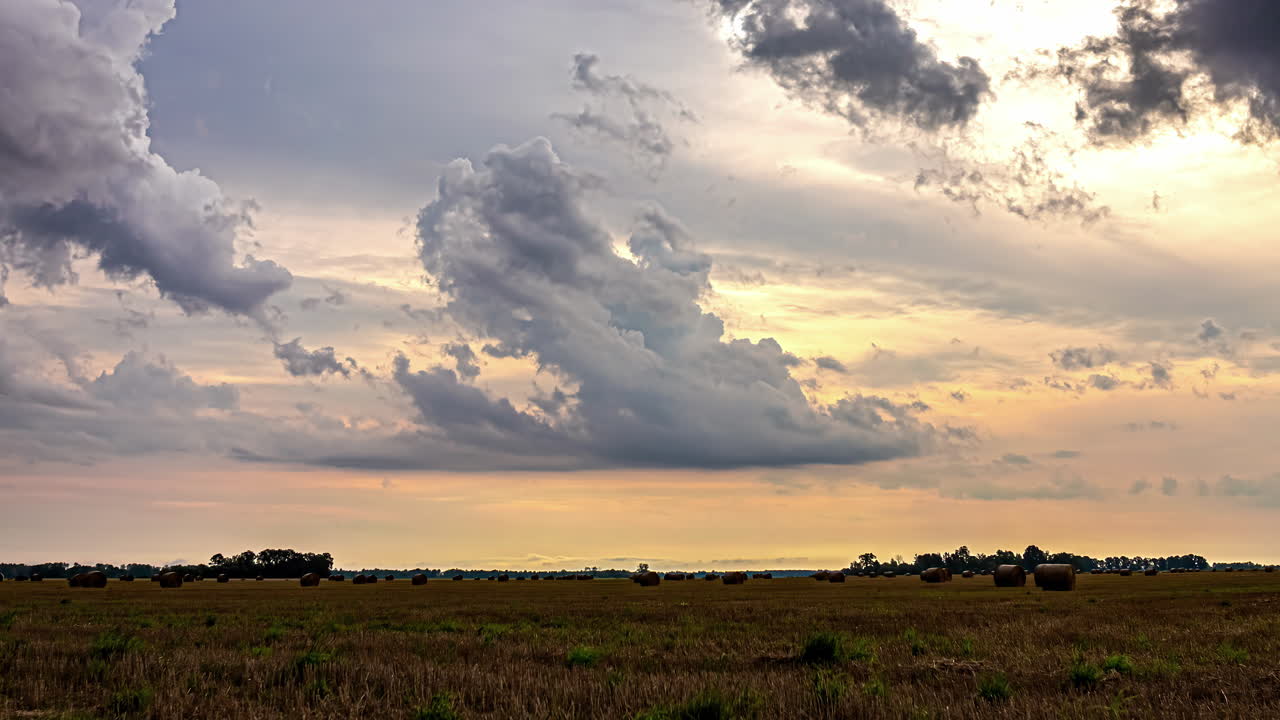 Timelapse shot of white clouds passing by over farmlands with haybales during evening time