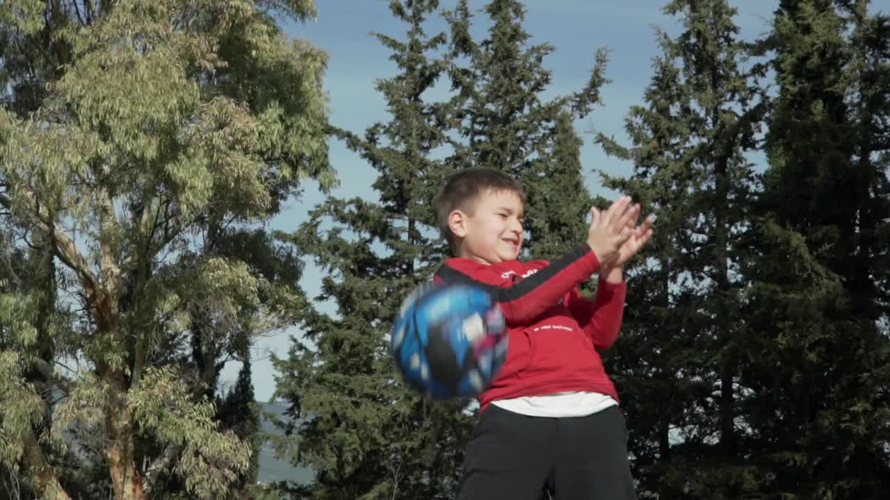 niño caucásico lanza la pelota de baloncesto al aire, grandes árboles forestales en el fondo 120fps