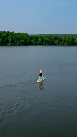 active adventure on water. sportsman training on water while standing on a board with oars on the background of beautiful summer landscape. extreme sport. vertical video