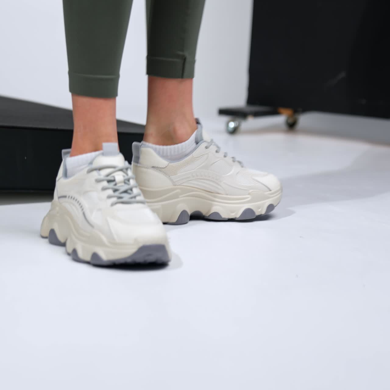 Model is fitting her trendy nice white sneakers. Fashionable comfortable footwear demonstrated in the studio
