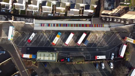 a slow rising, top down shot of a bus departing a bus station in a small colourful, city bus depot