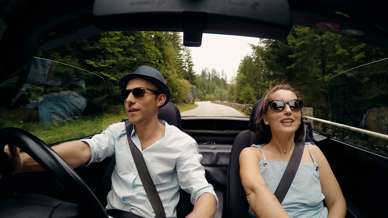 video en 4k: una pareja feliz canta las canciones mientras el coche descapotable sin techo conduce por el camino de la montaña.
