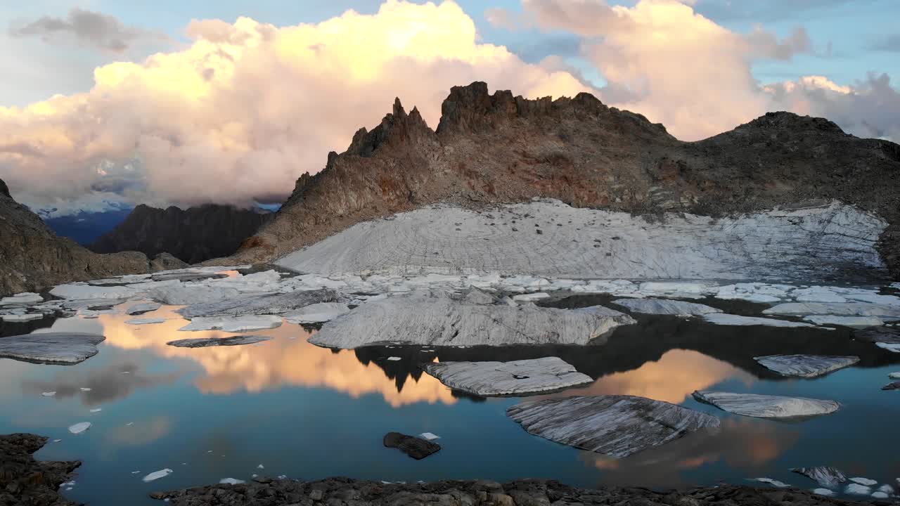 sobrevuelo aéreo sobre un lago lleno de icebergs de un glaciar que se derrite en partes remotas de los alpes suizos con nubes brillantes durante la puesta de sol