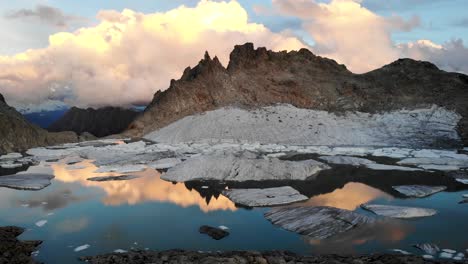 aerial flyover up above a lake full icebergs from a melting glacier in remote parts of the swiss alps with glowing clouds during sunset