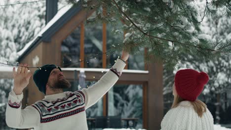 Caucasian-couple-decorating-garden-by-Christmas-in-lights-outdoors.