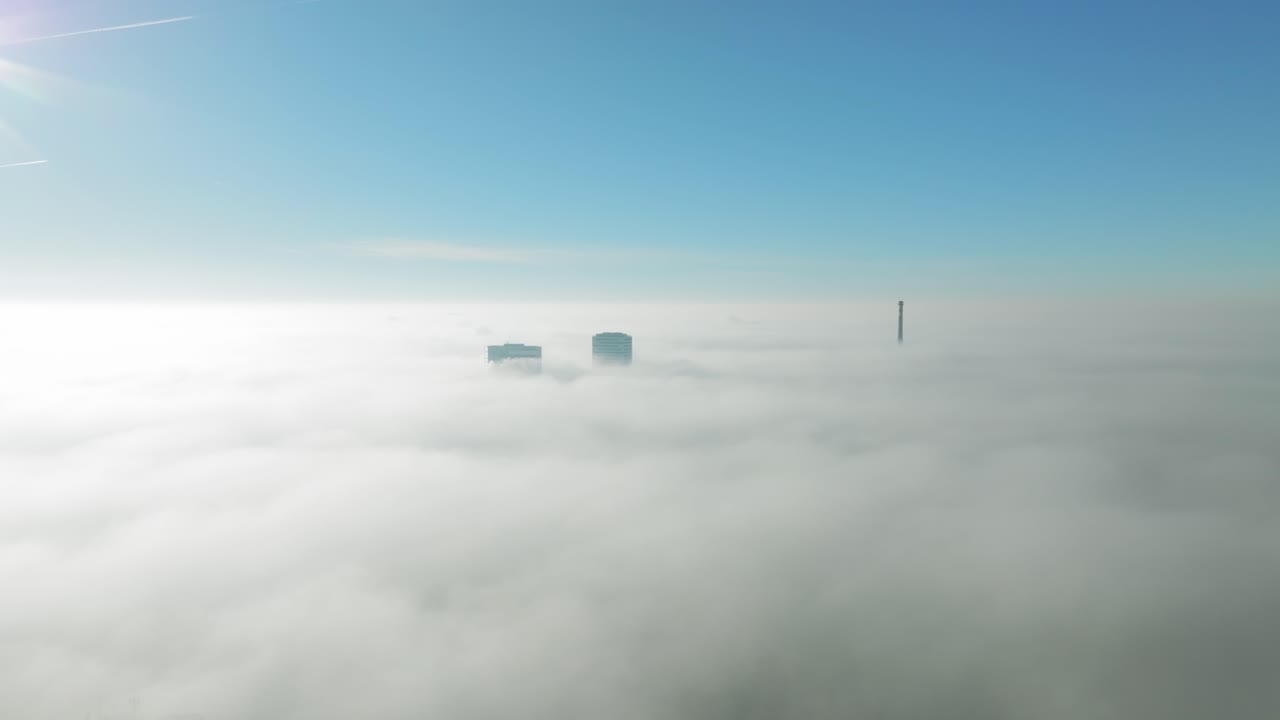 viaje aéreo de nubes invernales iluminadas por el sol: el avión no tripulado se mueve hacia adelante hacia altos rascacielos perforando a través de nubes de inversión revelando vistas de la ciudad