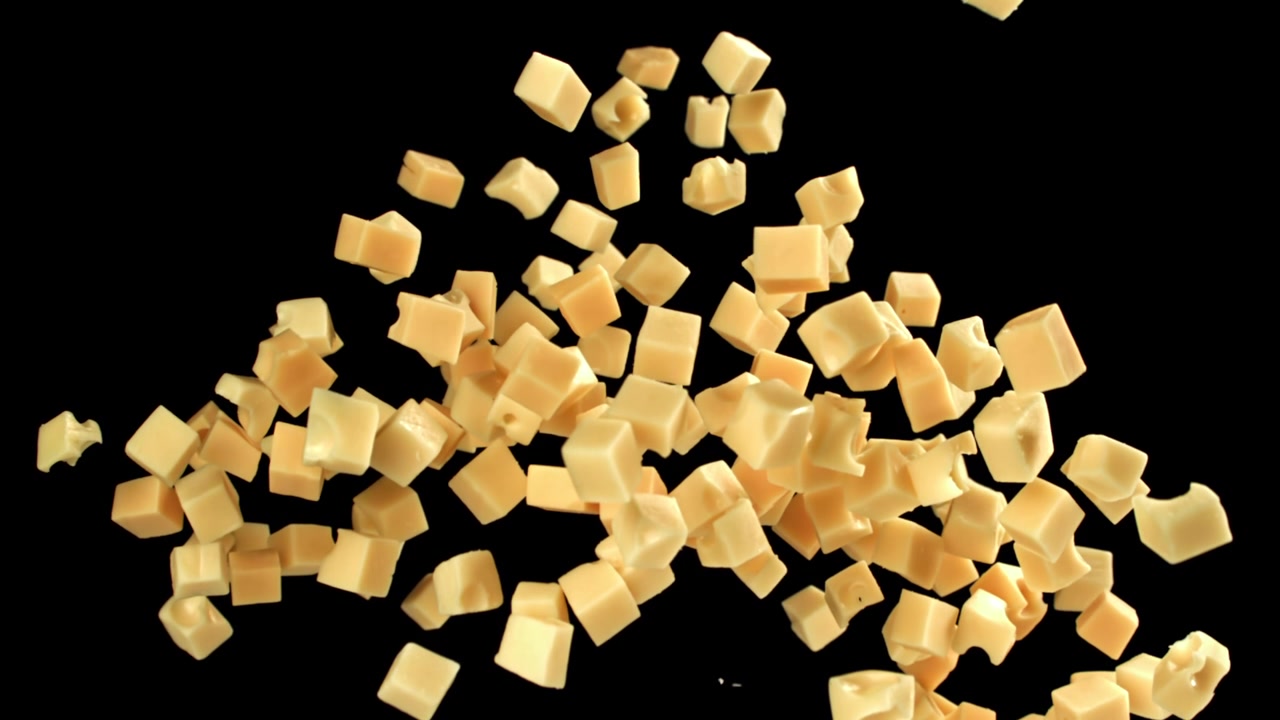 Movimento rallentato di cubetti di formaggio che cadono e si accumulano su sfondo nero.