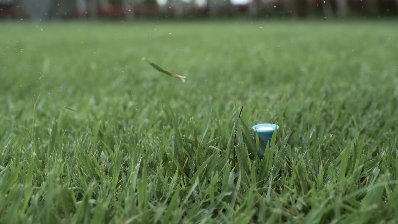 Golf club hits a white golf ball in a super slow motion. Drops of morning dew and grass particles rise into the air after the impact. Shot on super slow motion camera 1000 fps.