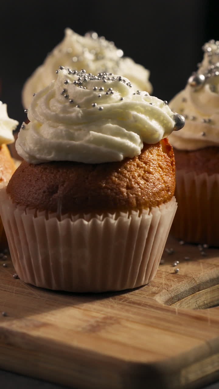 Vista verticale di cupcake ricoperti con glassa di panna montata e cosparsi di perle di zucchero lucide. Carrellata.