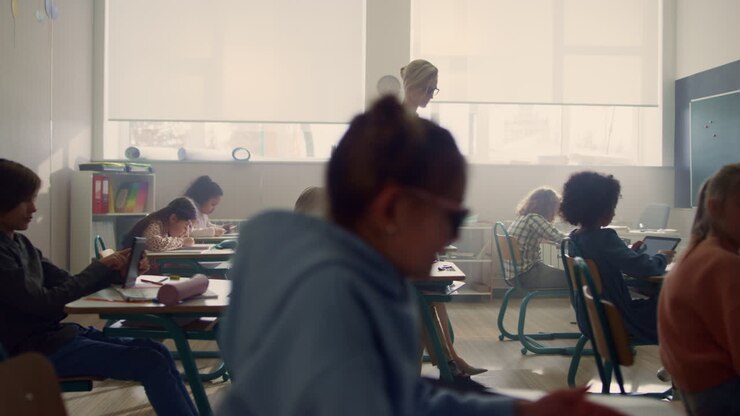 Een leraar loopt in de klas met leerlingen. Leerlingen maken een toets op tablets.