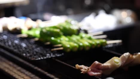 close up of yakitori, grilled skewered chicken, being cooked alongside green peppers