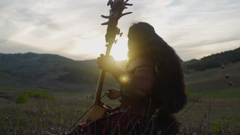 folk musician plays tovshuur with bow in mountain valley