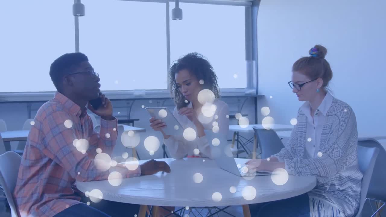 Animation of white spots of light over team of colleagues using electronic devices