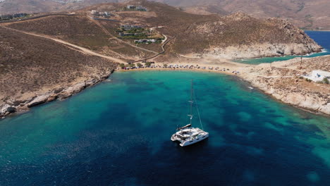 aerial pullback over agios sostis bay with vibrant blue water and remote beachscape below