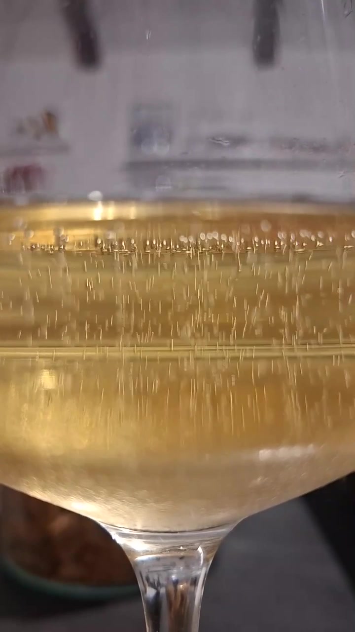 Primo piano verticale di bollicine di Prosecco che salgono nel bicchiere, vino spumante giallo paglierino